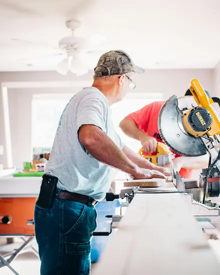 Homem cortando madeira numa serra, dentro de uma casa